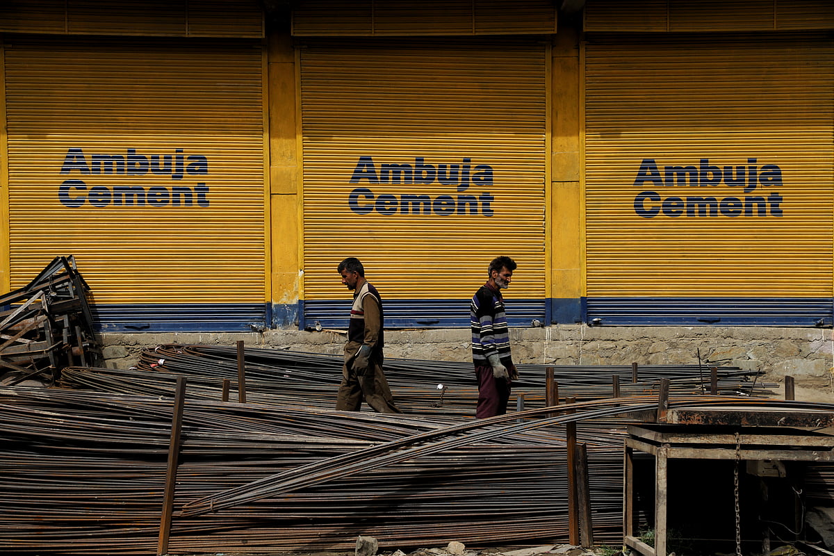 <div class="paragraphs"><p>Laborers carry iron rods as Ambuja Cement advertisement is seen on the closed shutters. (Photo by Nasir Kachroo/NurPhoto)<br></p></div>