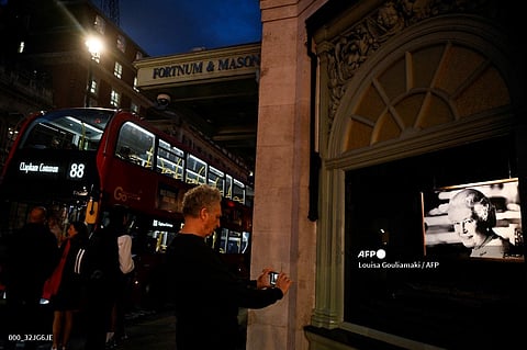 A pedestrian takes a picture of a photograph of late Queen Elizabeth II displayed as a tribute outside Fortnum and Mason shop, in central London on September 15, 2022, following the death of her Majesty on September 8. - Queen Elizabeth II will lie in state until 0530 GMT on September 19, a few hours before her funeral, with huge queues expected to file past her coffin to pay their respects. (Photo by Louisa Gouliamaki / AFP)