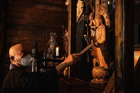 Buddhist monk Tesshu Inoue gestures toward a wooden statue holding grapes inside Daizenji temple, nicknamed the "grape temple", in Katsunuma in the city of Koshu, Yamanashi prefecture. - Daizenji, which sells its own table grapes and bottles of wine bearing the temple's name, is surrounded by vines cultivated in pergola, with head monk Tesshu Inoue being the honorary president of a local wine cooperative. Photo by Richard A. Brooks / AFP
