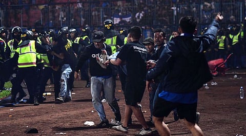 In this picture taken on 1 October 2022, a group of people carry a man at Kanjuruhan stadium in Malang, East Java, Indonesia, where at least 127 people died at a football stadium when fans invaded the pitch and police responded with tear gas. Photo by AFP