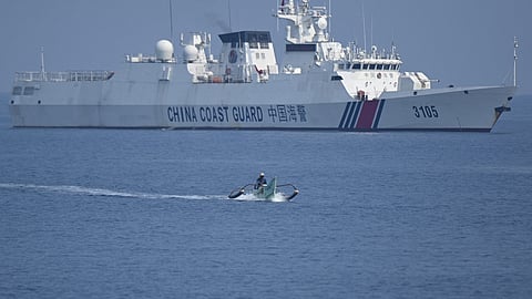 FILE: This photo taken on 20 September  2023 shows a Philippine fisherman aboard his wooden boat sailing past a Chinese coast guard ship near the Chinese-controlled Scarborough Shoal in disputed waters of the South China Sea. China, which claims sovereignty over almost the entire South China Sea, snatched control of Scarborough Shoal from the Philippines in 2012. Since then, it has deployed coast guard and other vessels to block or restrict access to the fishing ground that has been tapped by generations of Filipinos. 