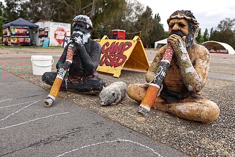 TWO statues of indigenous Australians with didgeridoos sit in front of the Aboriginal Tent Embassy located outside the old Parliament House in Canberra on 15 October 2023.  ~ DAVID GRAY/AGENCE FRANCE-PRESSE