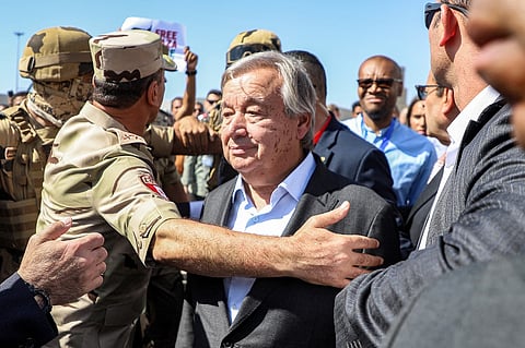 Protesters raise signs in solidarity with Palestinians in the Gaza Strip as Egyptian army officers and bodyguards escort United Nations Secretary-General Antonio Guterres to his vehicle during his visit to oversee preparations for the delivery of humanitarian aid to the Palestinian enclave on the Egyptian side of the Rafah border in the east of North Sinai province on October 20, 2023. (Photo by Kerolos SALAH / AFP)