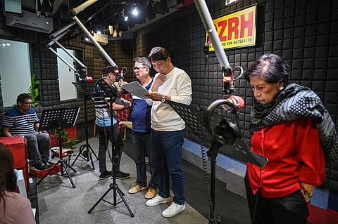 This photo taken on July 17, 2023 shows Phil Cruz (3rd L), his brother Robert (2nd R) and other voice actors recording their part for a radio drama at a studio of a radio station in Manila. Radio dramas were the main source of entertainment for Filipino families after World War II, just like the rest of the world, but their popularity faded with the rise of television, social media and video live-streaming. (Photo by TED ALJIBE / AFP) / To go with AFP story Philippines-entertainment-radio, FOCUS by Cecil MORELLA