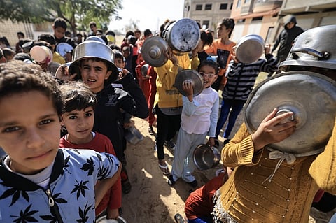 Displaced Palestinian children holding pots and pans wait in line as volunteers distribute a hot meal in Khan Yunis in the southern Gaza Strip on November 23, 2023. Photo by Mahmud HAMS / AFP