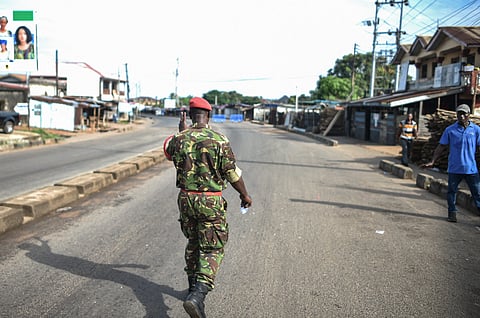A Soldier with the Sierra Leonean military police greets and man along an empty road in Freetown on 26 November 2023. A military armoury in Sierra Leone's capital Freetown came under attack on Sunday, the government said, as it imposed an immediate national curfew. (Photo by Saidu BAH / AFP)