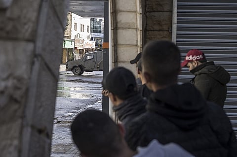 Palestinian youths observe an Israeli army patrol car from the safety of a corner at the entrance of the Jenin refugee camp in the occupied West Bank on December 13, 2023, as battles continue between Israel and the militant movement Hamas in Gaza. Photo by MARCO LONGARI / AFP