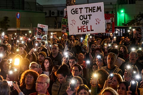Relatives and supporters light their phones around a placard reading "Get them out of hell" during a rally calling for the release of Israeli hostages held in Gaza since the 7 October attacks by Hamas in southern Israel, in Tel Aviv on 30 December 2023. (Photo by AHMAD GHARABLI / AFP)