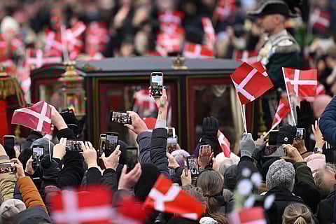 Queen Margrethe II of Denmark (unseen) rides in a carriage escorted by the Guard Hussar Regiment's Mounted Squadron from Amalienborg Castle to Christiansborg Castle as people raise flags and their mobile devices in Copenhagen, Denmark, on 14 January 2024, prior to her proclamation of abdication. Denmark turns a page in its history on 14 January when Queen Margrethe abdicates and her son becomes King Frederik X, with more than 100,000 Danes expected to turn out for the unprecedented event. (Photo by Jonathan NACKSTRAND / AFP)