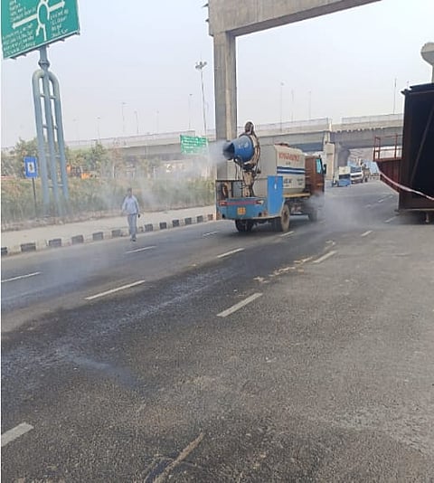 A truck-mounted anti-smog gun spraying a fine water mist over a Delhi highway as a pedestrian walks nearby.