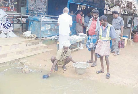 கறம்பக்குடி பஸ் நிலைய சாலையில் தேங்கிய மழைநீரை பாத்திரத்தில் அள்ளி அகற்றும் துப்புரவு தொழிலாளர்கள்