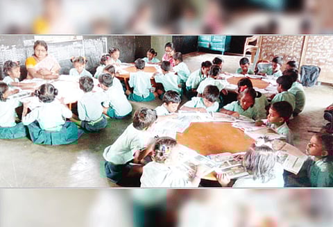 அரசு பள்ளியில் வட்ட மேஜையை சுற்றி மாணவர்களுடன் தரையில் அமர்ந்து பாடம் கற்பிக்கும் ஆசிரியைகள்