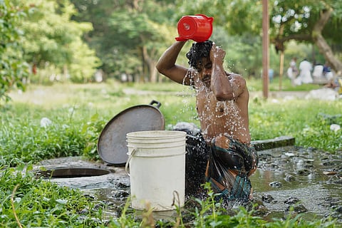 A man pours water over his head beside a roadside drain in Dhaka