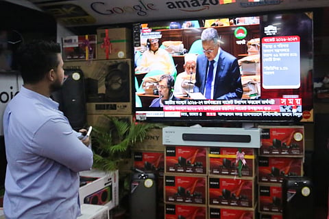 People watch from a roadside shop as Finance Minister Amir Khasru Mahmud Chowdhury announces the national budget for fiscal year 2026–27 in the Jatiya Sangsad on Thursday. 