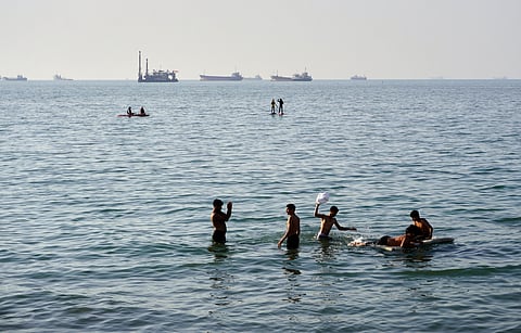 Residents swim and play in the waters of the Strait of Hormuz while cargo ships and commercial vessels lie anchored in the distance off Bandar Abbas, Iran, Wednesday, June 10, 2026. 