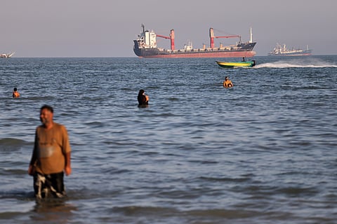 Residents swim in the waters of the Strait of Hormuz as a small motorboat passes cargo ships and other commercial vessels offshore near Bandar Abbas, Iran, 17 June 2026. 