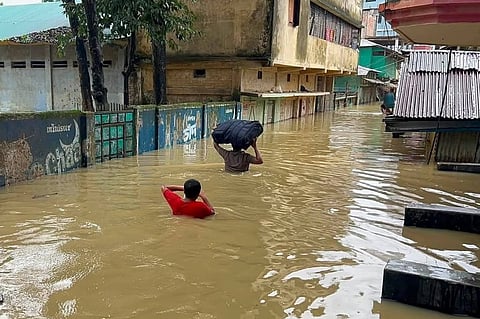 People are seen wading through waist-deep, muddy water to evacuate or transport essential belongings safely out of the flooded zones in Bandarban.