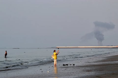 A woman stands at the water’s edge along the Strait of Hormuz as a plume of smoke rises in the background following an explosion off Bandar Abbas, Iran, on 13 July, 2026.