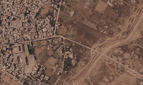 This satellite image from Planet Labs PBC shows a section of an earthen barrier being built by the Israeli military, right side of image moving top to bottom, in the central Gaza Strip, July 1, 2026. At left is the Maghazi refugee camp, and on the other side are homes demolished by the military.