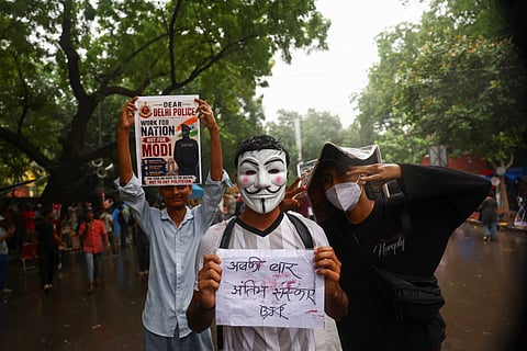 A supporter of India's Cockroach Janta Party (CJP) while wearing a Guy Fawkes mask holds a piece of paper with a message at Jantar Mantar in New Delhi, India on July 22, 2026.