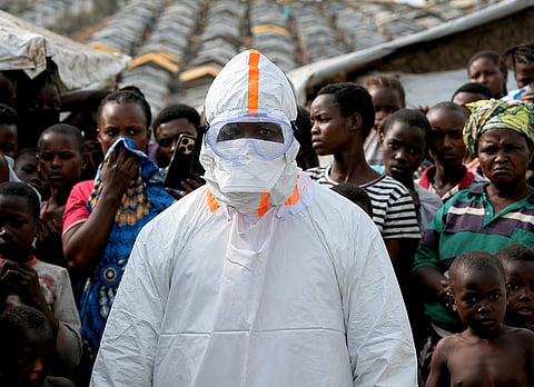 A health worker in personal protective equipment stands near displaced people waiting for the burial of suspected Ebola victims at the Kigonze displaced persons camp, one month after an outbreak was declared, in Bunia, eastern Democratic Republic of Congo, June 18, 2026.