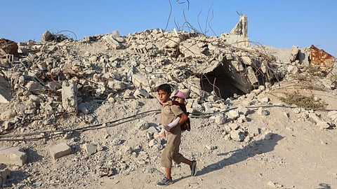 A Palestinian boy carries a younger child past the rubble of buildings destroyed in Israeli strikes in Gaza. 