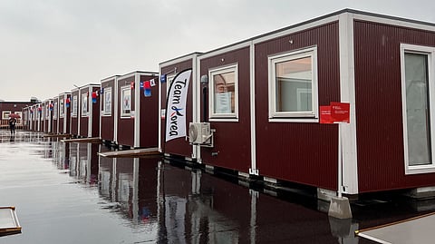 A person walks near wooden container-style huts built to house athletes, including South Korean athletes, at Athletes Plaza of Aichi-Nagoya Asian Games 2026 in Nagoya, central Japan, September 27, 2026.