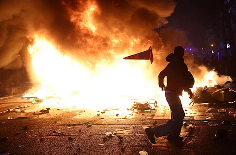 A man throws a plastic traffic cone through a burning barricade amid clashes during a day of demonstrations against the cost of living and rising fuel prices in Paris as part of nationwide protests called by the "Yellow Vests" movement, joined by French high school and university students, teachers and parents demanding better school conditions and government action, as well as labour unions, workers, farmers and retirees, France, October 17, 2026. 