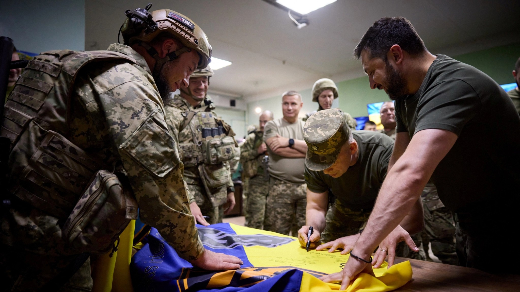 Ukraine's President Volodymyr Zelenskyy assists while Commander of the Ground Forces colonel general Oleksandr Syrsky signs a national flag during their visit to a position of Ukrainian service members at a front line near the town of Bakhmut, amid Russia's attack on Ukraine, in Donetsk region, Ukraine September 5, 2023. 