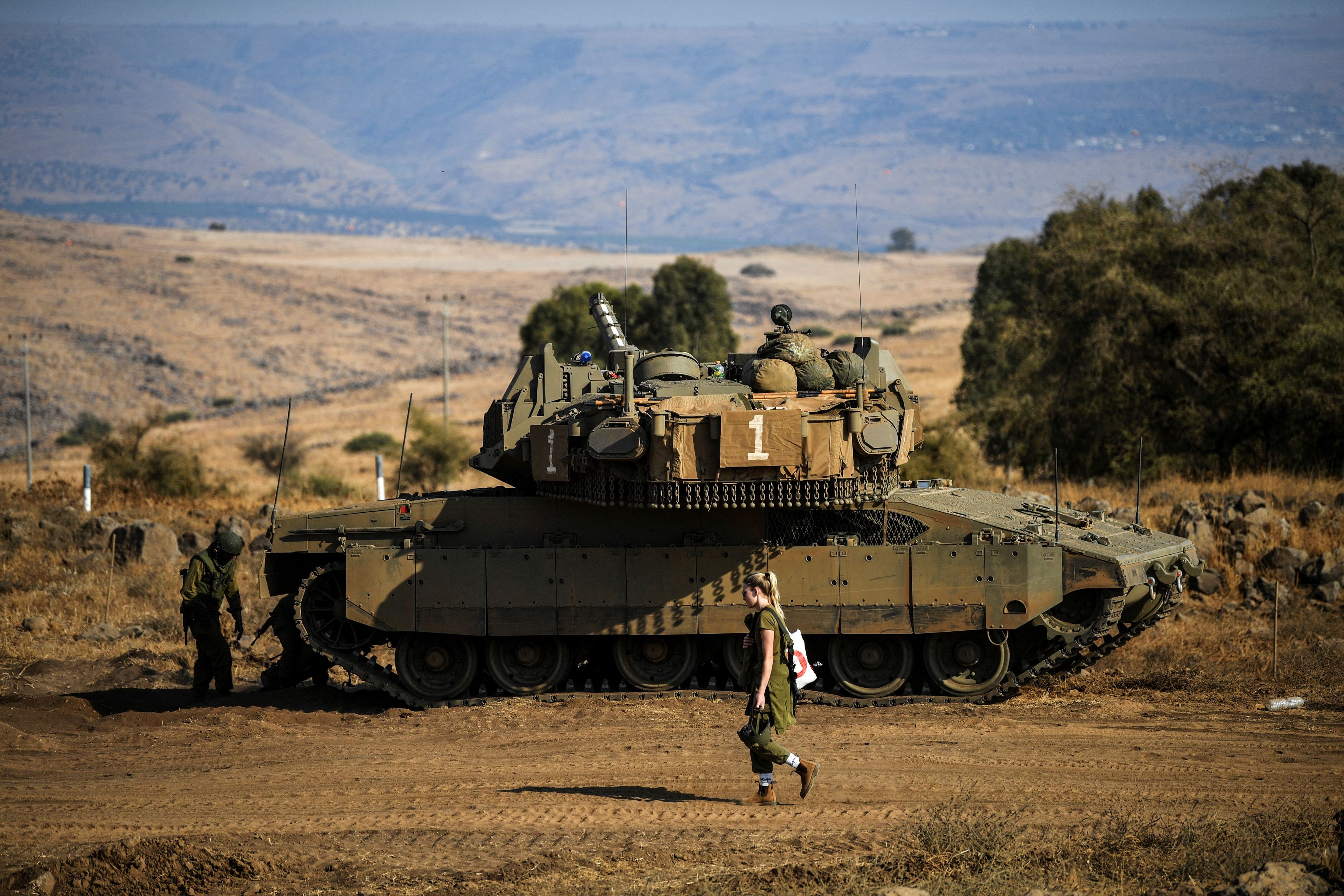 An Israeli soldier walks past a tank amid heightened tensions between Israel and Lebanon, as seen from the border with Lebanon in northern Israel, October 14, 2023. 