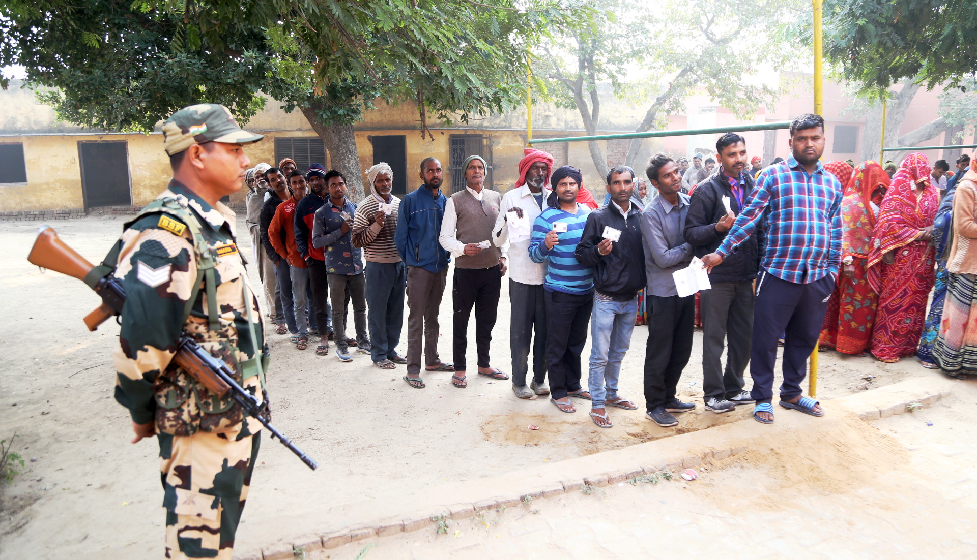 A security personnel stand guard as people wait to cast their votes for the Rajasthan Assembly elections, in Bharatpur district, Saturday, November 25, 2023.