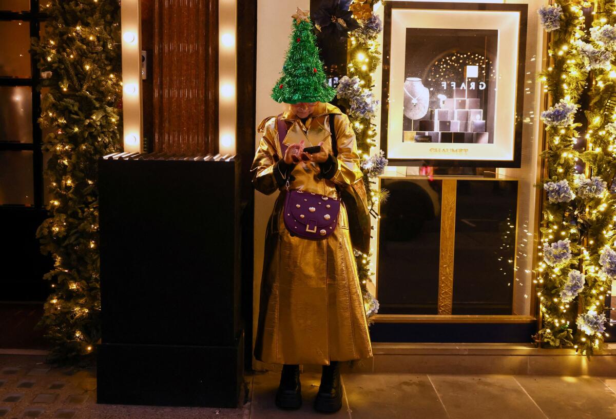 A woman wearing a Christmas tree hat uses her phone outside a shop on Bond Street in London.