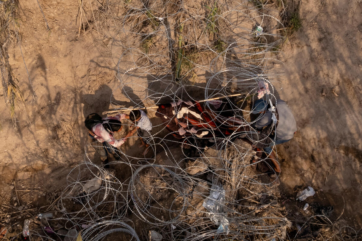 A migrant child crawls out through concertina wire along the banks of the Rio Grande River while crossing from Mexico into Eagle Pass, Texas