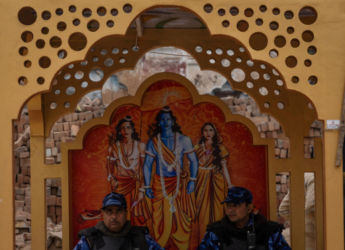 Members of Rapid Action Force (RAF) sit in front of a painting of Hindu Lord Ram, his wife Goddess Sita and younger brother Laxman on a street ahead of the opening of the grand temple of Lord Ram in Ayodhya in India, January 19, 2024