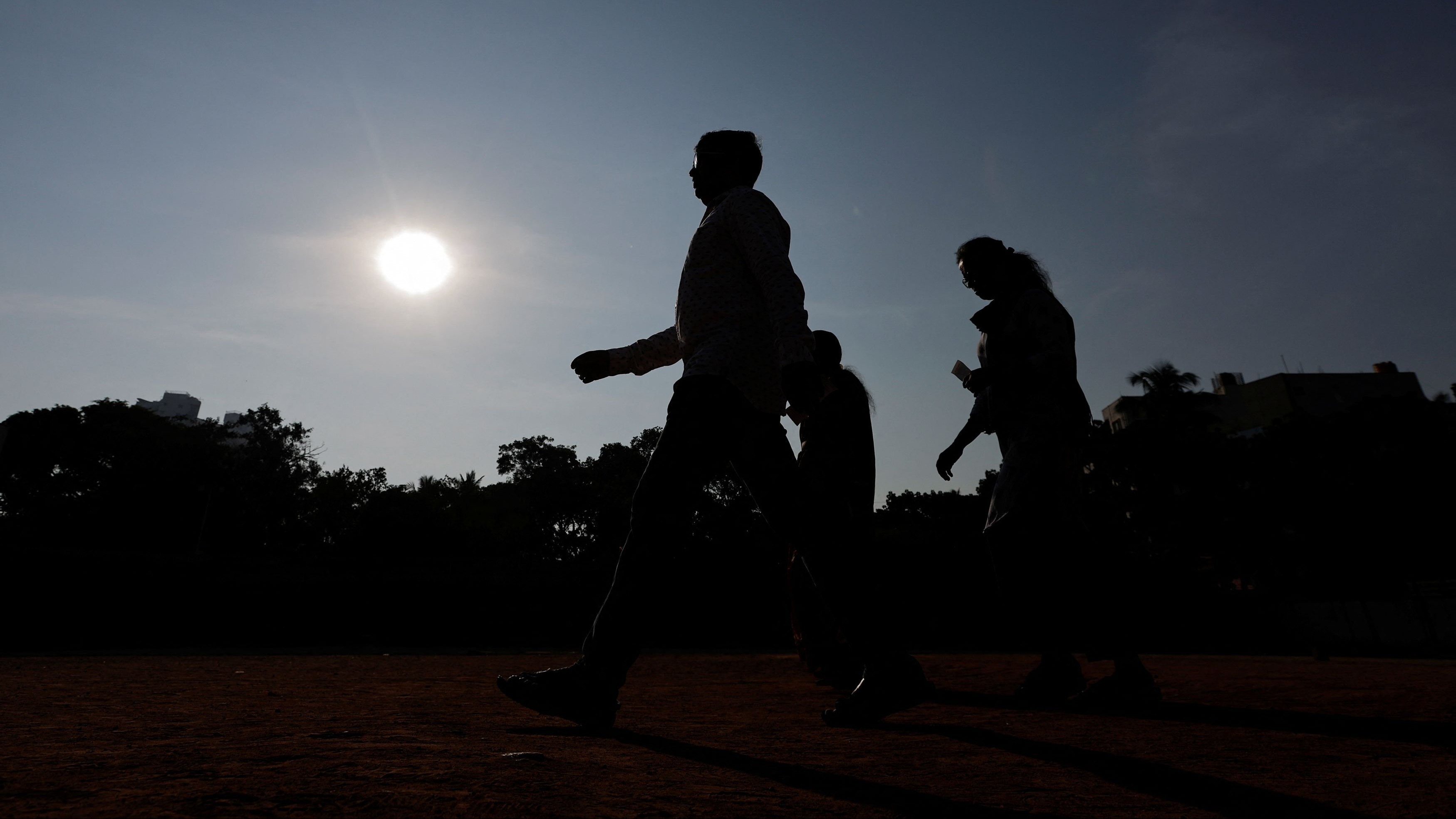 People are silhouetted against the sun as they walk outside a polling station during the second phase of the general elections, at Bengaluru, in Karnataka, April 26, 2024. 
