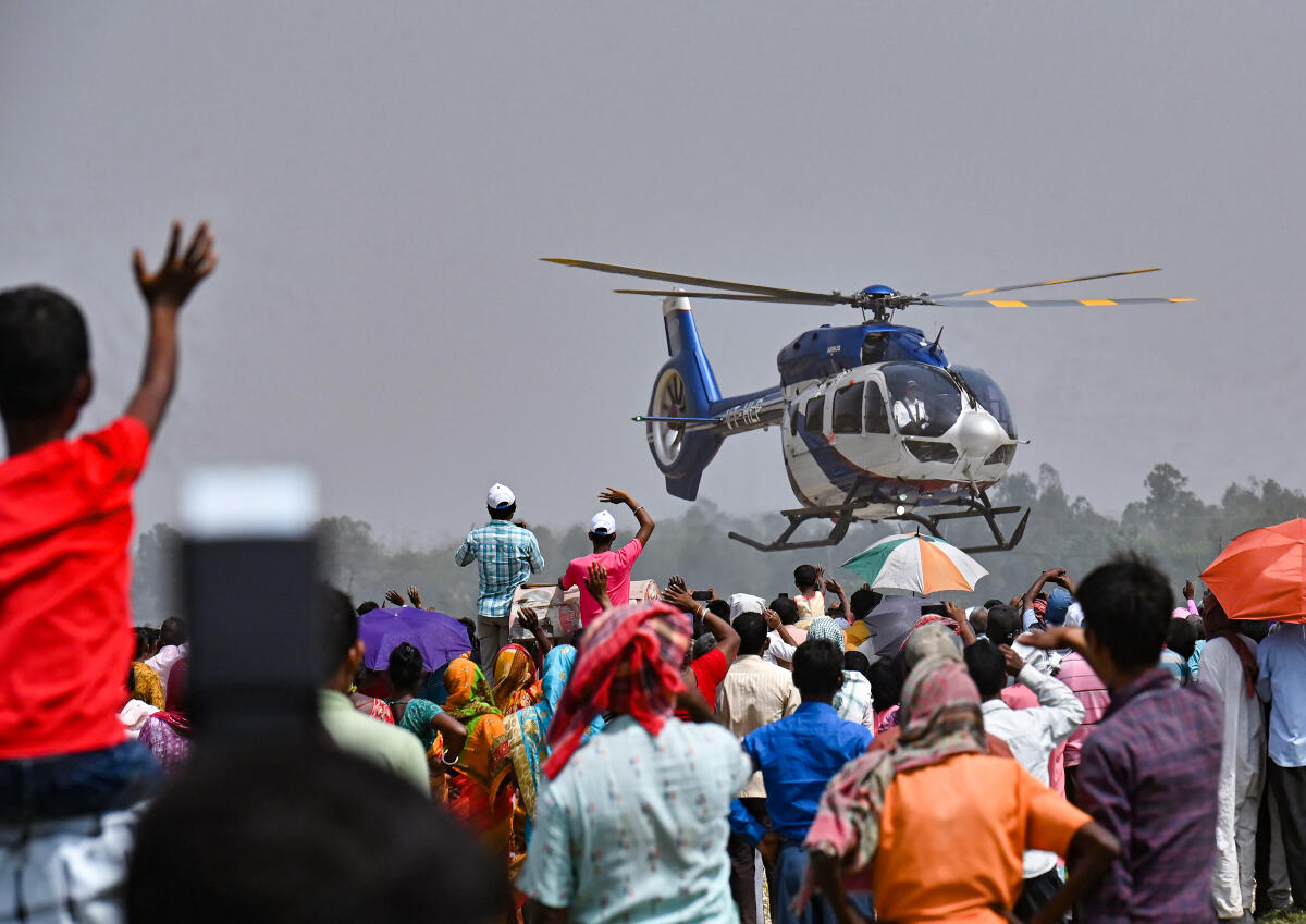 People wave at West Bengal Chief Minister and TMC chief Mamata Banerjee's helicopter during a public meeting, ahead of Lok Sabha elections, at Tapan in South Dinajpur district, Saturday, April 6, 2024.