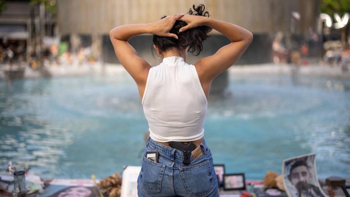 A woman carries a gun in a waistband holster, as she stands next to pictures of hostages kidnapped during the deadly October 7 attack by the Palestinian Islamist group Hamas, at Dizengoff Square in Tel Aviv, Israel, May 23, 2024.