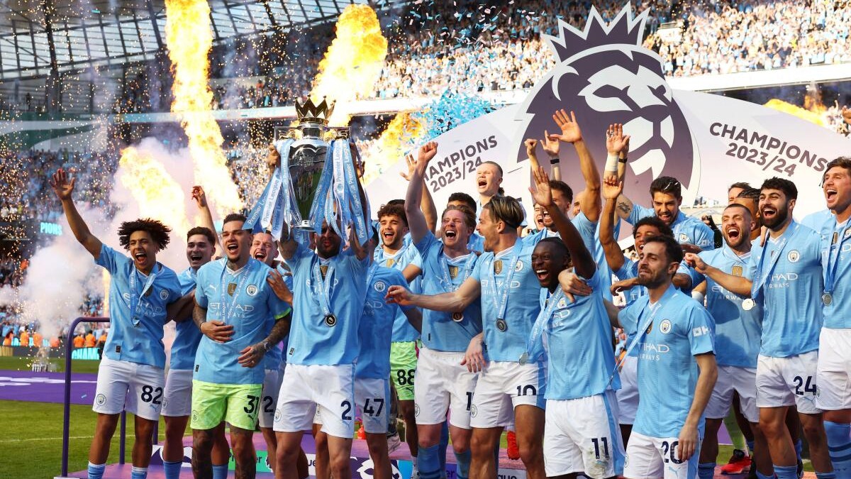 Manchester City's Kyle Walker lifts the trophy on the podium and celebrates with teammates after winning the Premier League.