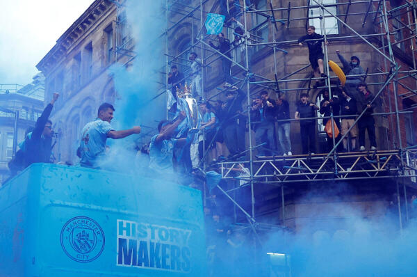 Manchester City's Ruben Dias holds the Premier League trophy as Rodri and Matheus Nunes celebrate on the bus during the victory parade
