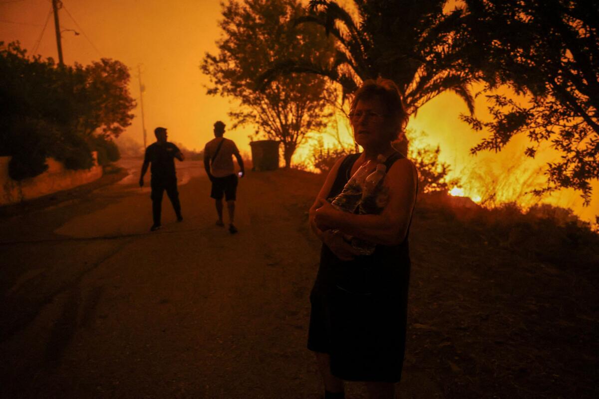 A local resident holds bottles of water next to a wildfire burning in the village of Latas, in southern Greece, June 21, 2024.