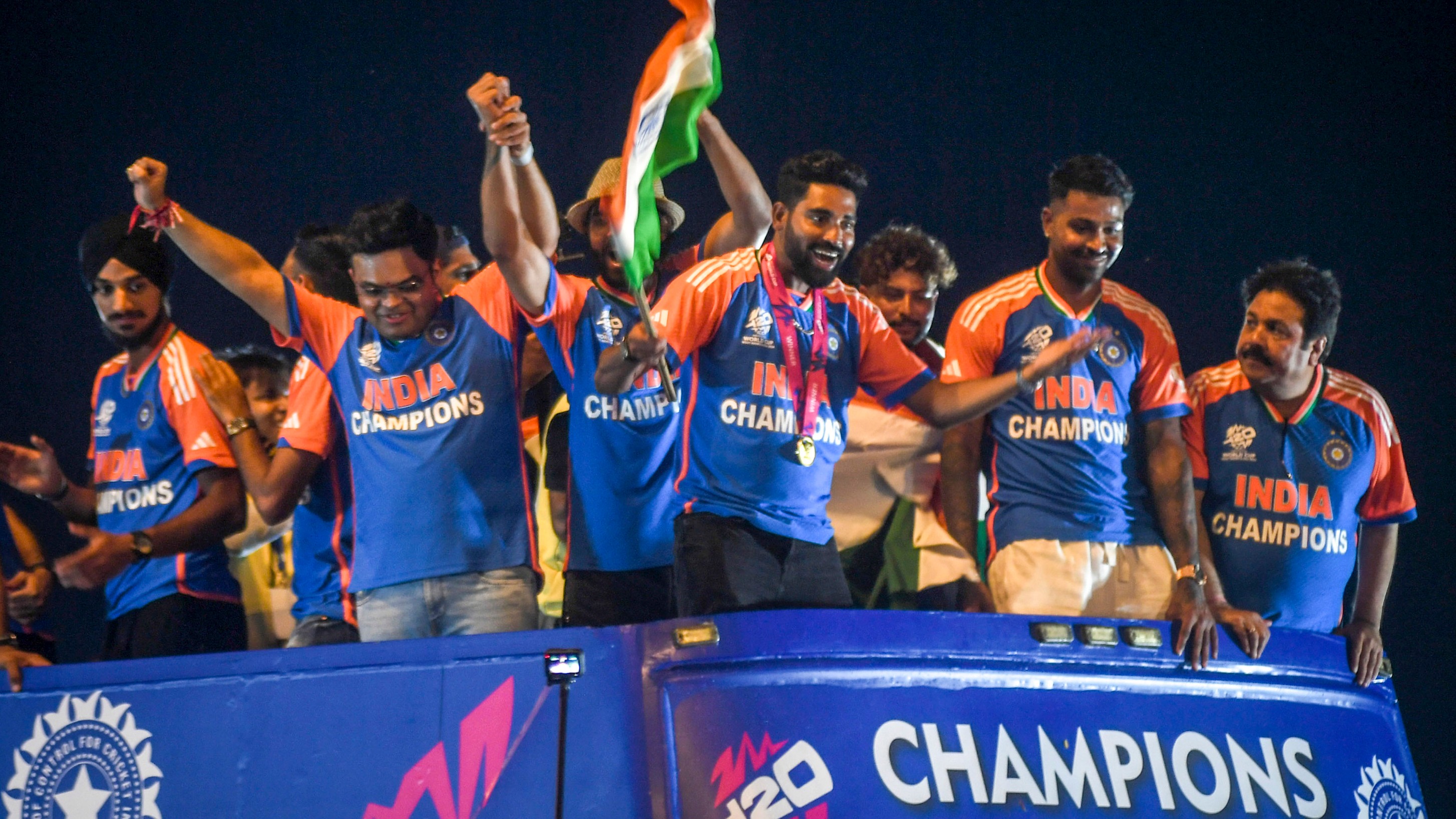 Players of the T20 World Cup-winning Indian cricket team with the championship trophy acknowledge fans during their open bus victory parade, in Mumbai.
