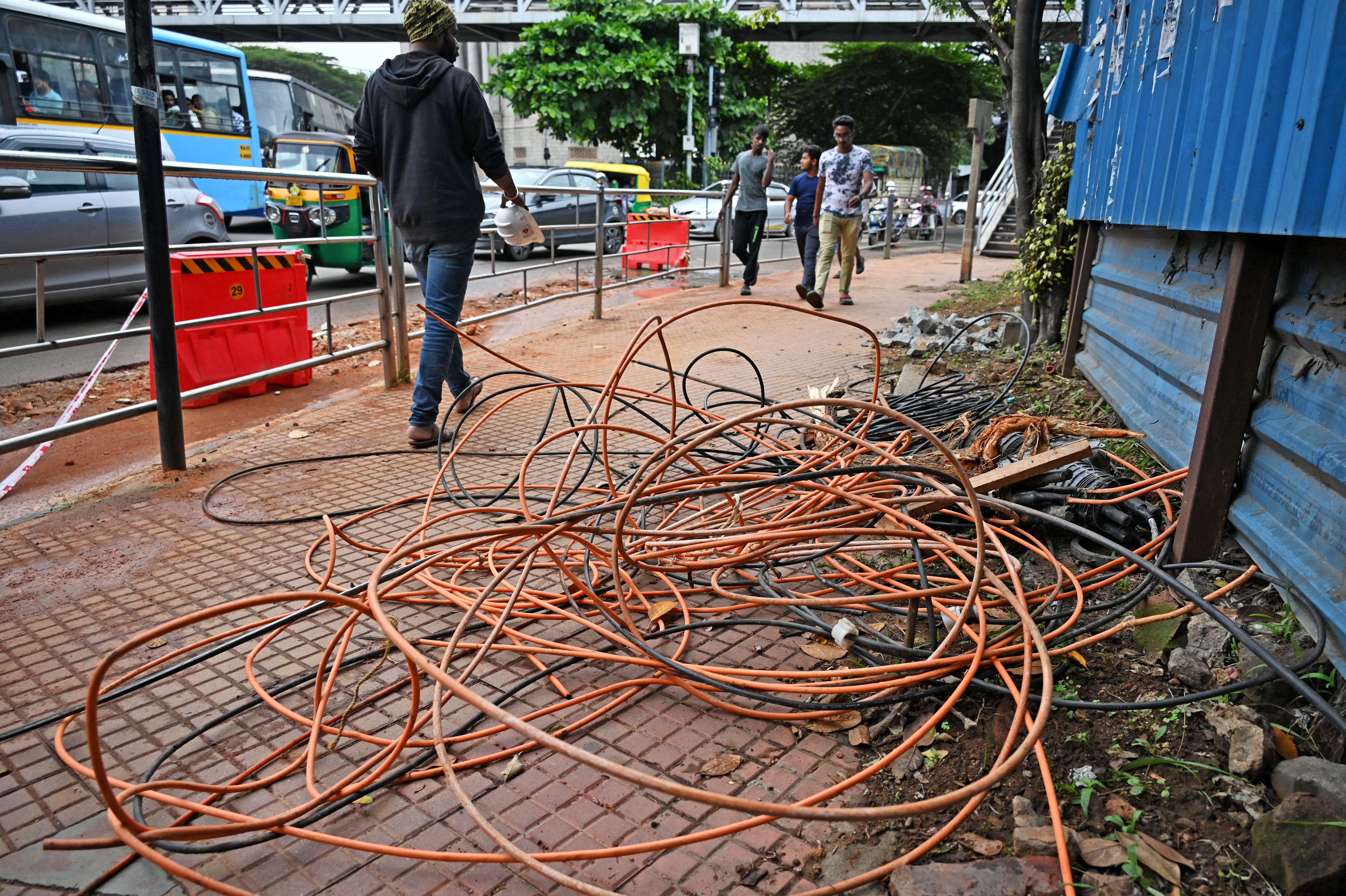 Pedestrians walk past bundled optical fibre cables occupying the footpath near the Halasuru Gate traffic police station.