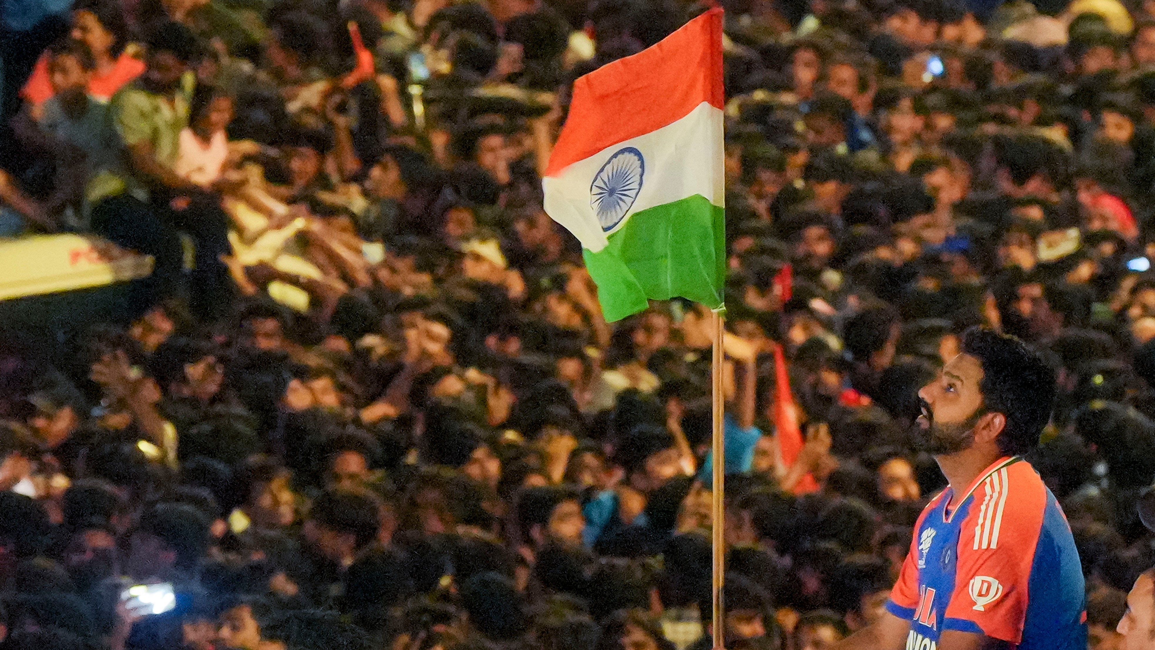 The T20 World Cup-winning Indian cricket team captain Rohit Sharma holds the tricolour during the open bus victory parade, in Mumbai.