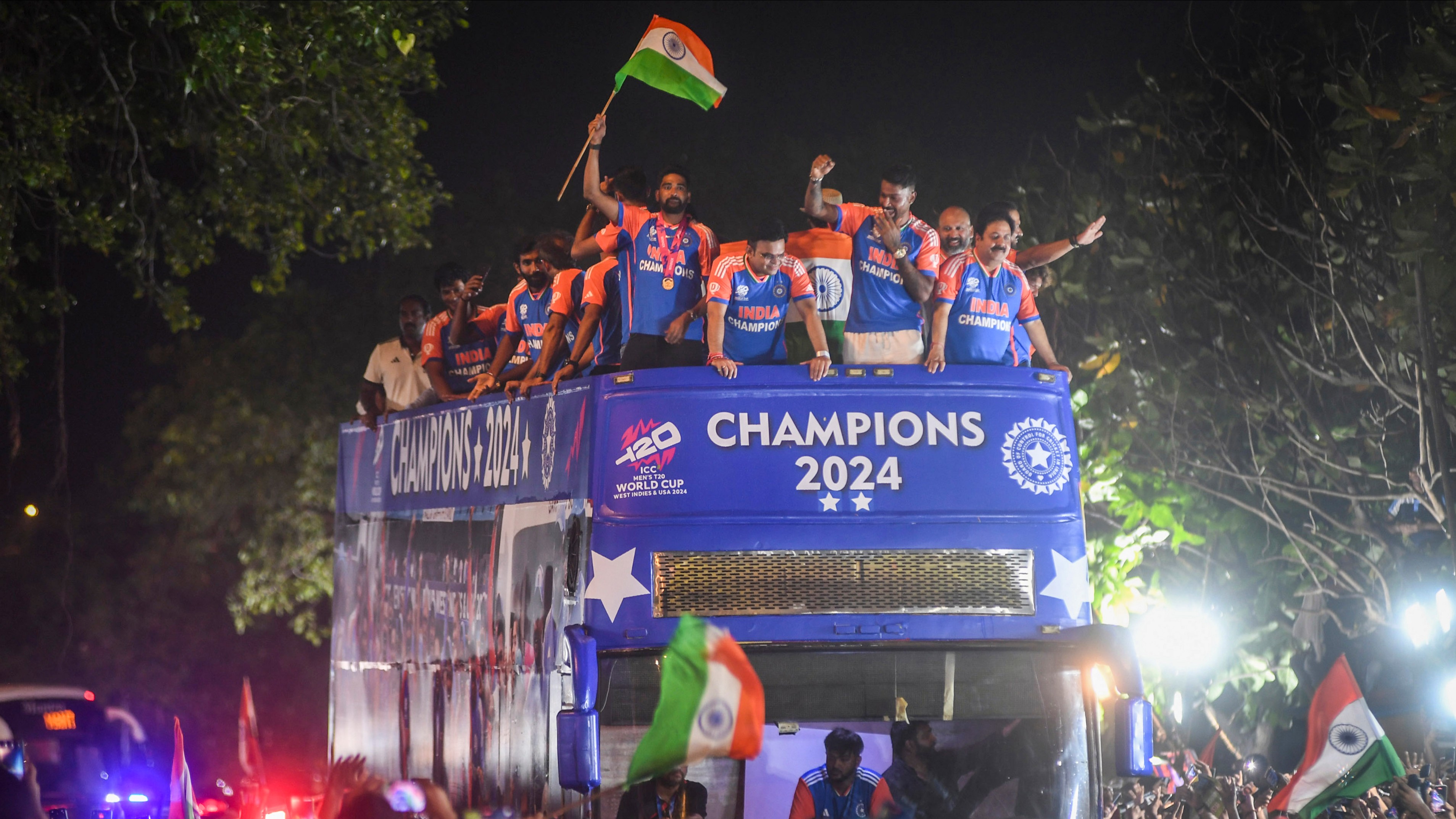 Players of the T20 World Cup-winning Indian cricket team with the championship trophy acknowledge fans during their open bus victory parade, in Mumbai.
