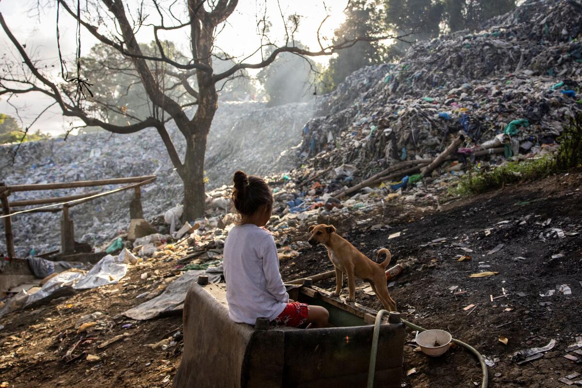 A girl sits next to a dog near a garbage dump filled with plastics in Rodriguez, Rizal province, Philippines.