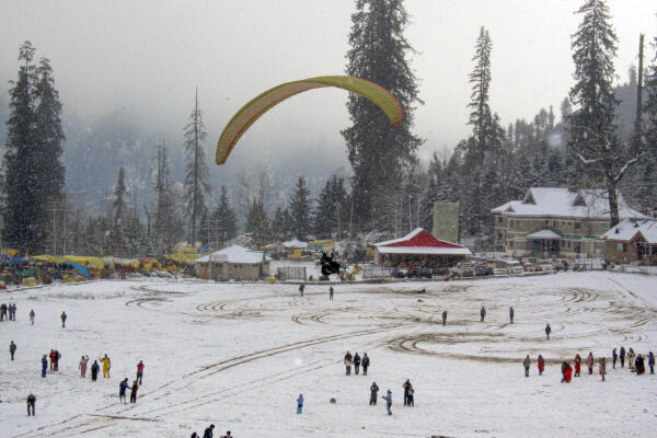 Tourists participate in paragliding amidst fresh snowfall in Solang valley, in Manali district