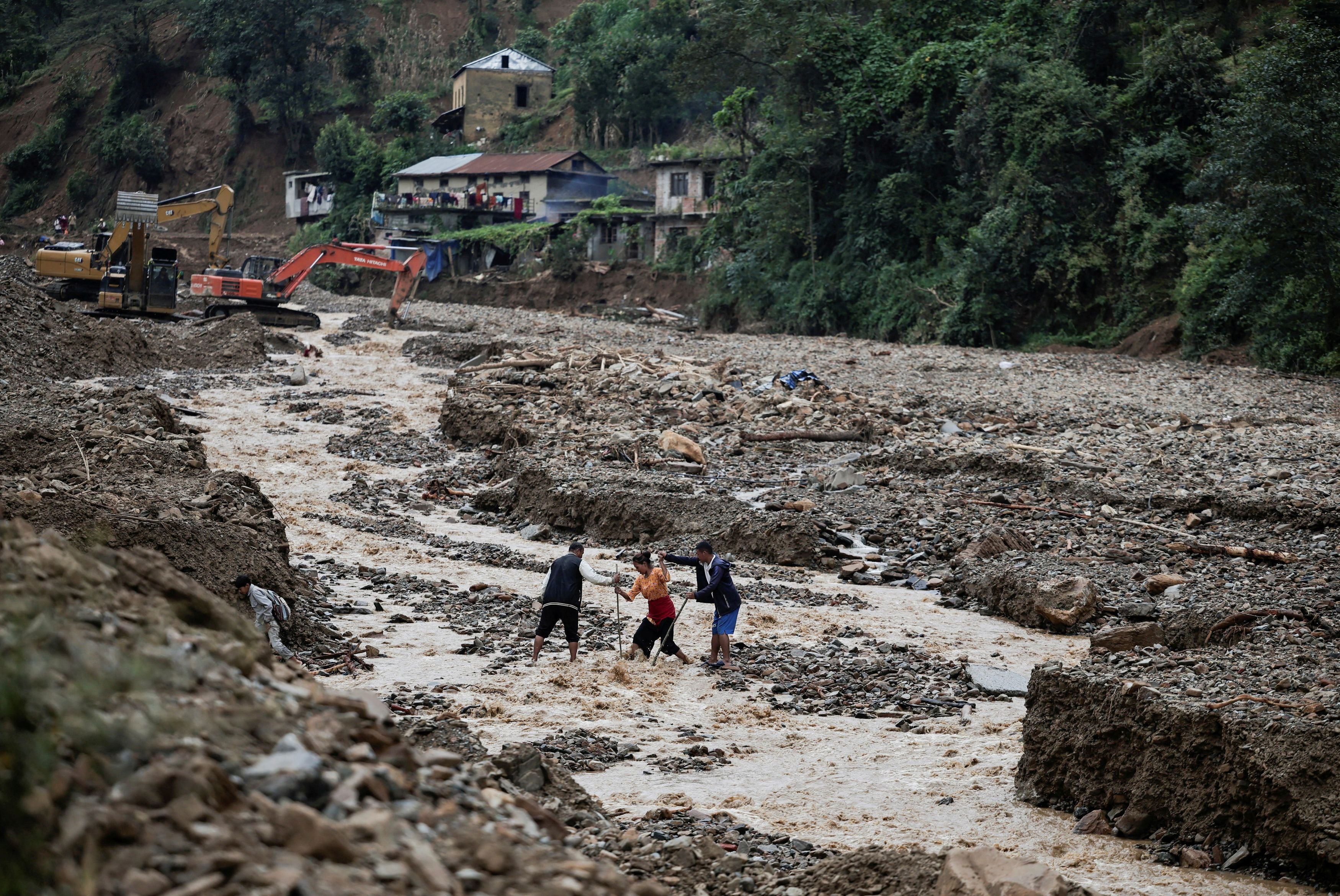People cross a river after the deadly floods following heavy rainfall, in Bethanchowk, Kavre, Nepal.