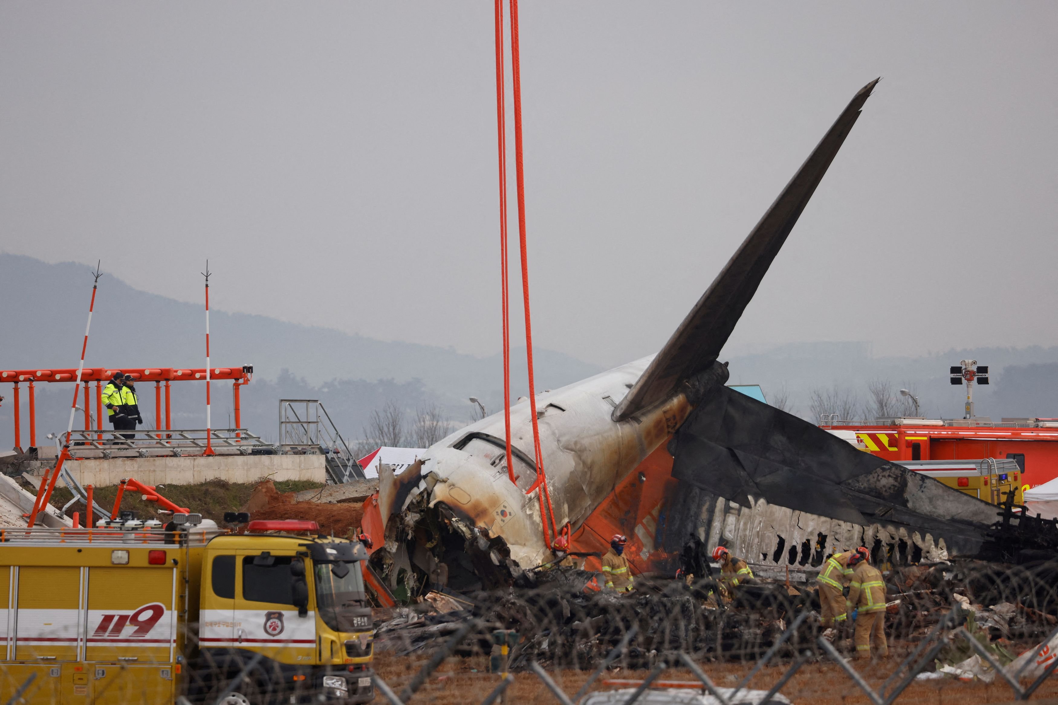 People stand as the wreckage of an aircraft lying on the ground after it went off the runway and crashed at Muan International Airport is pictured, in Muan, South Korea.