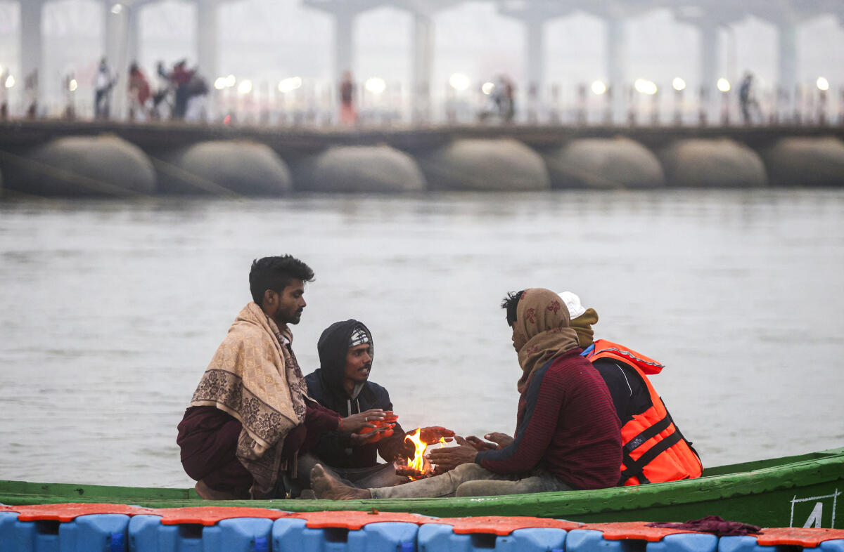 People warm themselves around a bonfire on the banks of the Ganga river during the ongoing ‘Maha Kumbh Mela’ festival, in Prayagraj, Uttar Pradesh.