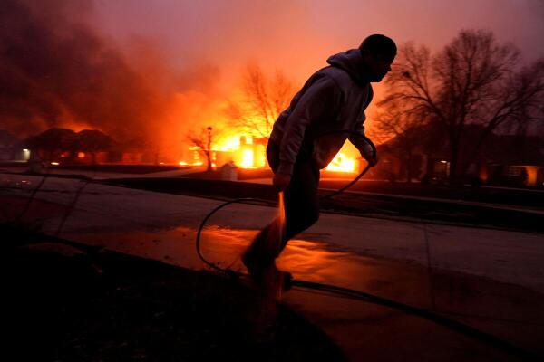 Cody McIntire runs as he sprays water on a fire burning in a yard in front of his friend's house during a wildfire outbreak in Stillwater, Oklahoma.